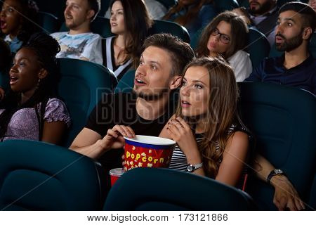 Lost their breath Young loving couple looking shocked as they are watching a movie at the local movie theatre together