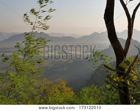 View from mountain mount zwegabin in valley below during sunrise with sun rays beams shining through the fog and mist in the valley