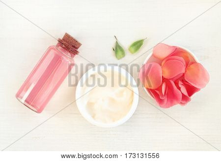 Skincare herbal cosmetics daily set, top view. Jar of cream, pink rose petals, facial tonic in bottle.