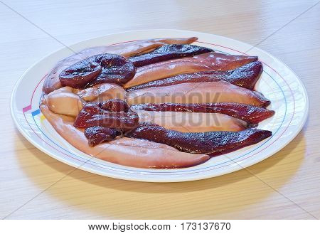 raw eggs and milt in the bag of herring lie horizontally in a ceramic white dish on wooden table