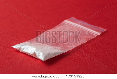 Cocaine in plastic packet on red background, closeup. Portion of drugs