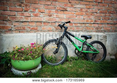 Children's old green Bicycle near brick wall and flowers