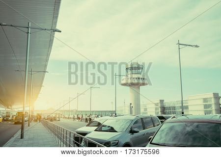 Parking lot and road near modern contemporary airport terminal in front of air traffic control tower with many passengers and staff passing in distance Barcelona Spain