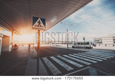 Pedestrian crossing next to contemporary modern airport terminal entrance zebra traffic cross way with road sing with parking lot and small buses in distance on sunny day in Barcelona Spain