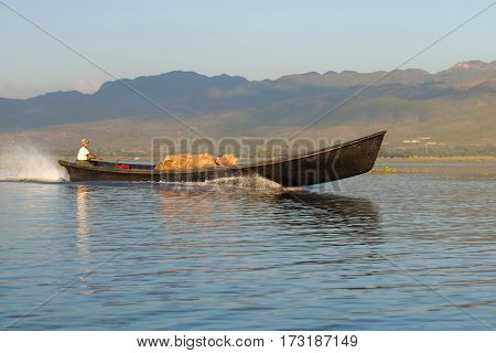 INLE LAKE, MYANMAR - DECEMBER 26, 2016: The boatman is transporting wooden boxes on the boat