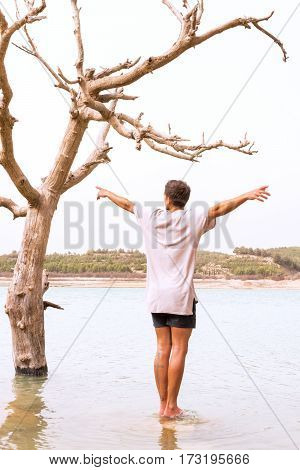 conceptual image of climate change. young man mimics the dying tree in a lake that has been floodedfilter added blank sky in background for copy space