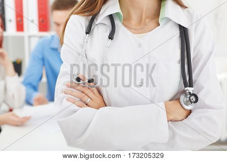 Female medicine doctors's hands crossed on her chest closeup with family couple on the background. Medical help or insurance concept. Doctor is waiting for patient to examine. Physician reception concept