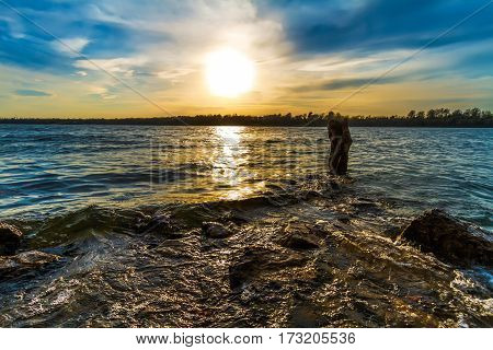 Sunset at Lake Jacomo just outside of Kansas City Missouri. it is shot horizontal with waves going over a rock and around a stump in the water