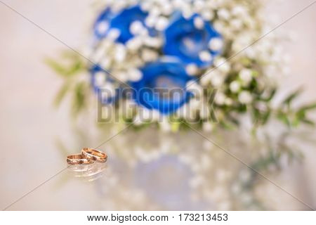 Wedding rings on a glass table next to the beautiful blue bouquet with reflection