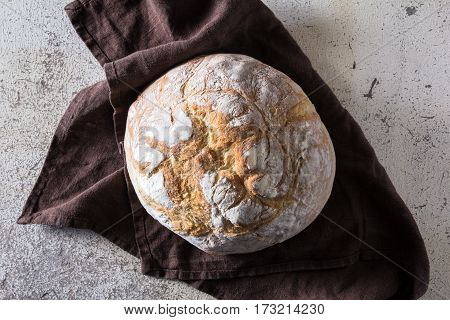 Freshly baked traditional bread liying on brown kitchen towel on white rustic background. View from above