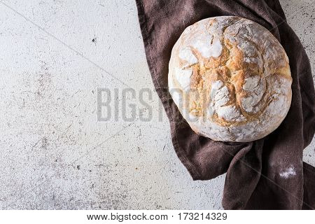 Freshly baked traditional bread liying on brown kitchen towel on white rustic background. View from above