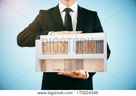 Businessman holding modern house on light blue background. Property concept. 3D Rendering