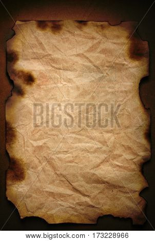 old crumpled sheet of paper with burnt edges on a dark brown background closeup