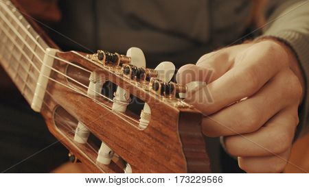 Guitarist's hands tuning the acoustic guitar close-up
