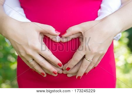 the parents hold the tummy in the form of heart on a background of red dress