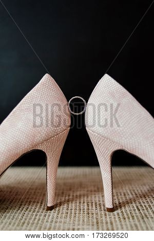 Wedding ring is between the bride's shoe on a dark background.