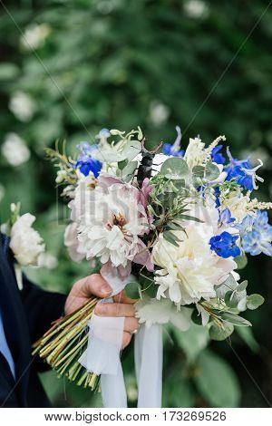 The groom holding a wedding bouquet of peonies on which stag beetle sitting