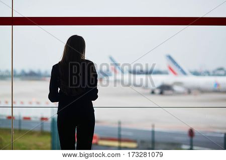 Woman With Hand Luggage In International Airport, Looking Through The Window At Planes