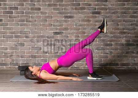 Slim fitness young woman doing plank corp exercise in front of brick wall.