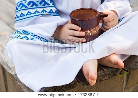 Children's picnic with dairy products and pancakes. Children in the Russian national clothes on a picnic. Rural food. Food background. The child in national clothes holds in hand a clay mug with milk.