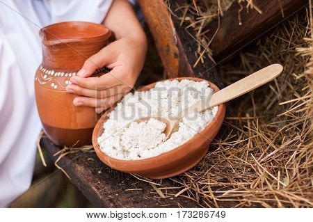 Picnic with dairy products and pancakes. Cottage cheese in pottery against the background of dry hay. The hand of the child holds a clay jug with milk. Rural food. Food background.