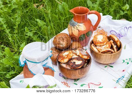 Dairy products on the embroidered white cloth. Cheesecake and milk on the table in an earthenware dish. Rural food. Food background. Picnic with dairy products and pancakes.