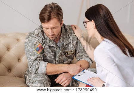 Psychological help. Pleasant nice female psychologist holding her hand on the patients shoulder and trying to help him while having a psychological session