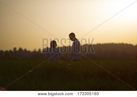 couple walking through the field and holding hands over sunset