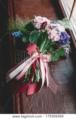 Tenderless bouquet with bow and ribbons in green and pink and blue colours on brown background