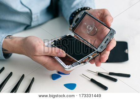 Repairman disassembling smartphone close-up. Male hands holding opened mobile phone for diagnostics, repair tools on workplace. Electronic fixing, modern technology, business concept