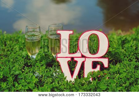 Glasses with champagne and homemade wooden plaque with the word love in the grass are beautiful