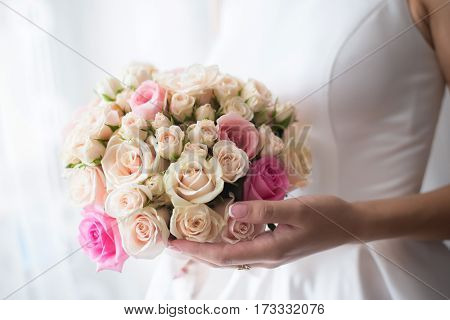 Beautiful wedding bouquet of delicate beige roses in hands of bride