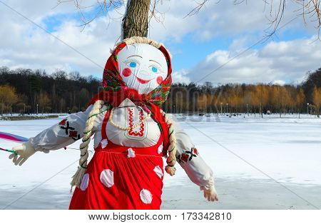 Shrovetide doll in colorful headscarf and sarafan on background of spring landscape