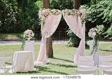 Arch for the wedding ceremony, decorated with cloth, flowers and greenery, in front of trees