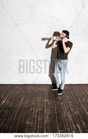 Vertical image of Hipster in snap back drinking wine and talking on phone