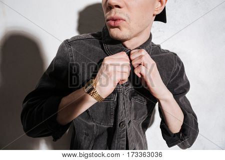 Cropped image of hipster in jeands shirt posing near the wall and buttoning