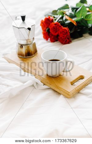 A cup of coffee coffee on the wooden Boards a bouquet of red roses on a white rumpled bedding greeting early in the morning
