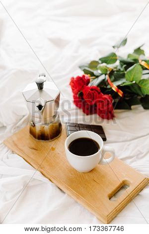 A cup of coffee coffee on the wooden Boards a bouquet of red roses on a white rumpled bedding greeting early in the morning