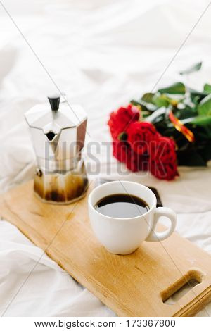 A cup of coffee coffee on the wooden Boards a bouquet of red roses on a white rumpled bedding greeting early in the morning