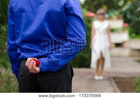 Groom hiding the wedding ring behind his back and going to offer it to a bride. Surprise proposal concept