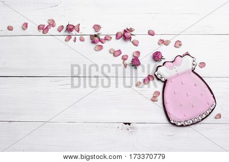 Cookies With Glaze In The Form Of Dress With Flying Petals Of Dried Roses. On White Wooden Surface.