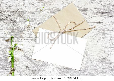 blank white greeting card and envelope with snowdrop flowers over rustic table with copy space. mock up