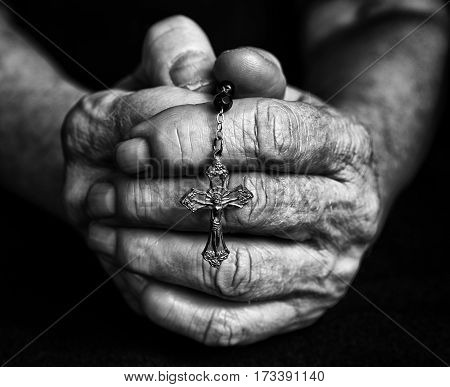Rosary in old closed hands together. Black and white fotography