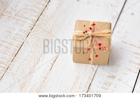 Gift box wrapped in craft paper tied with twine tender small red flower white plank wood background minimalistic copyspace kinfolk top view