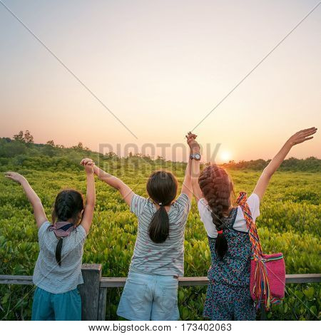 Tree Asian sister young girls holding hands and watching sunset at Tung Prong Thong Golden Mangrove Field Klaeng Thailand.