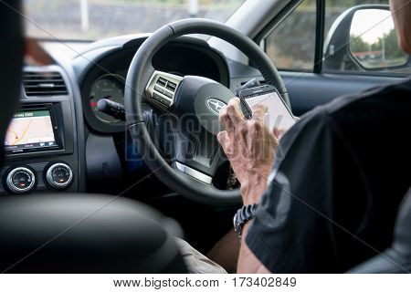 Lopburi province Thailand - January 14 2017 : Asian man stop driving and using a smartphone. Car driver use gps mobile app for traveling. Focus on hand holding cellphone.