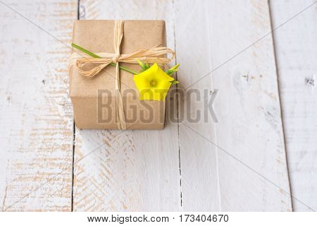 Gift box wrapped in craft paper tied with twine spring yellow flower white plank wood background minimalistic copyspace kinfolk top view