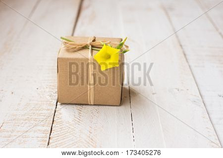 Gift box wrapped in craft paper tied with twine spring yellow flower white plank wood background minimalistic copyspace kinfolk