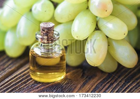 Healing grapes seeds oil in a glass jar, fresh grapes on old wooden background, seed extract has antioxidant and nourishing the skin, spa concept, selective focus macro front view. Bio, eco products.