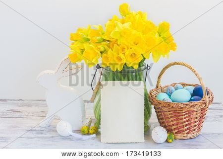 Easter eggs hunt - white rabbit, basket with painted eggs and daffodils bouquet, copy space on white paper note